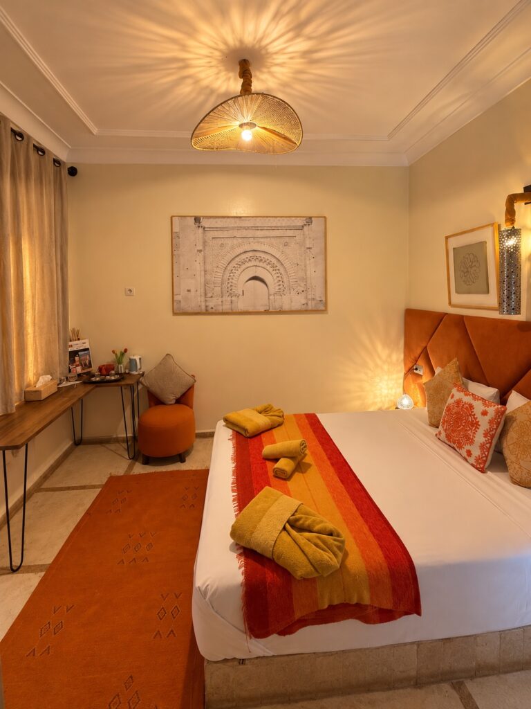Chambre Almohades : coin salon, fauteuil orange et bureau près de la fenêtre.